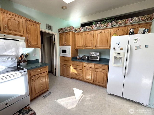 kitchen with dark countertops, visible vents, range hood, brown cabinets, and white appliances