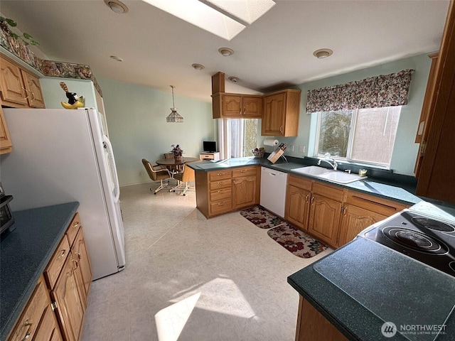 kitchen with light floors, vaulted ceiling with skylight, a peninsula, white appliances, and a sink