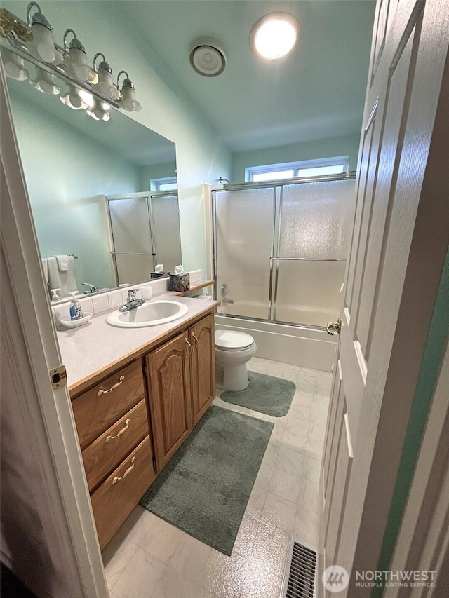 bathroom featuring tile patterned floors, visible vents, toilet, combined bath / shower with glass door, and vanity