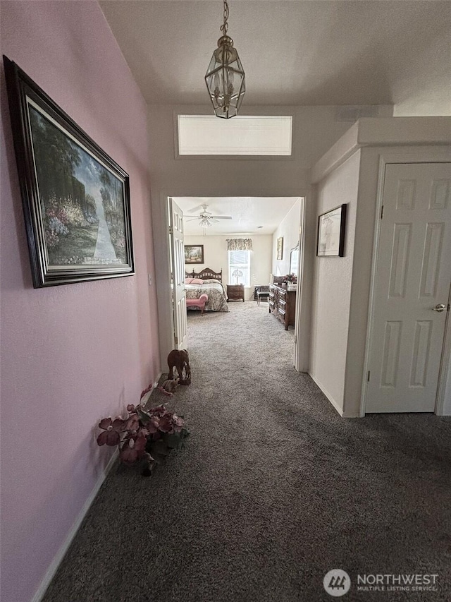 hallway featuring a notable chandelier, carpet flooring, and baseboards