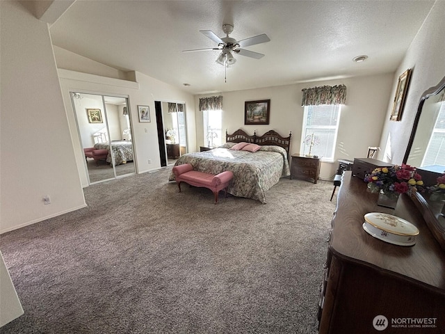 bedroom featuring lofted ceiling, ceiling fan, multiple closets, a textured ceiling, and carpet flooring