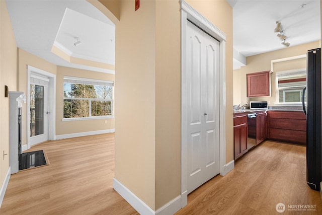 hallway with crown molding, baseboards, a tray ceiling, light wood-style floors, and arched walkways