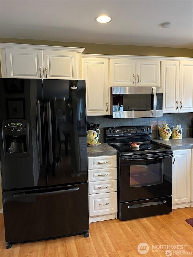 kitchen with dark countertops, backsplash, light wood-type flooring, white cabinets, and black appliances