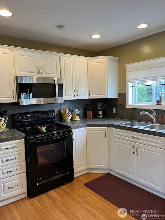 kitchen with light wood finished floors, stainless steel microwave, a sink, and black electric range