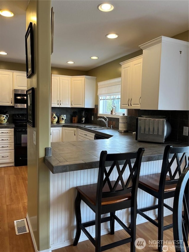 kitchen with stainless steel microwave, black range with electric cooktop, a breakfast bar, light wood-style floors, and a sink