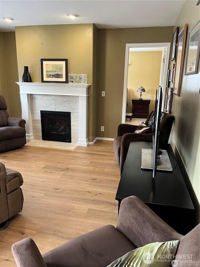 living room featuring baseboards, light wood-style flooring, and a tiled fireplace