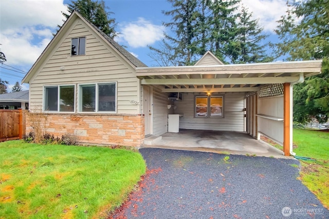 view of front of home with an attached carport, fence, driveway, stone siding, and a front lawn