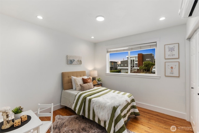 bedroom with recessed lighting, a wall unit AC, baseboards, and wood finished floors