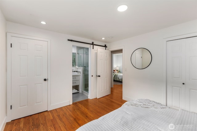 bedroom featuring a closet, recessed lighting, wood finished floors, and a barn door