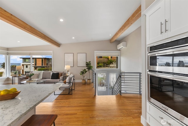 kitchen featuring a wall unit AC, open floor plan, light stone countertops, stainless steel double oven, and beam ceiling