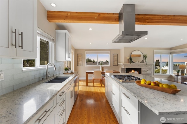 kitchen featuring light stone counters, stainless steel appliances, a sink, white cabinetry, and island exhaust hood