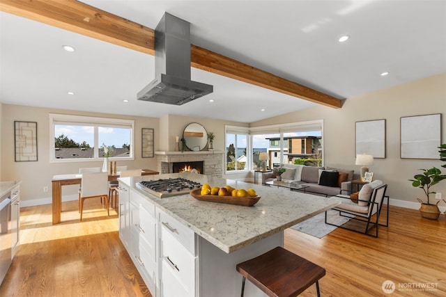 kitchen with island exhaust hood, a kitchen island, open floor plan, and light stone counters