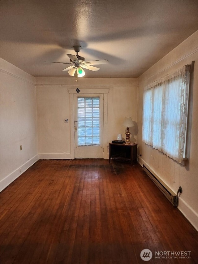 interior space featuring a baseboard heating unit, a ceiling fan, plenty of natural light, and dark wood-style floors