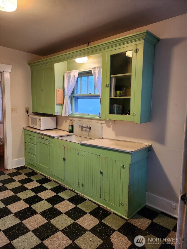 kitchen featuring dark floors, light countertops, green cabinetry, and white microwave