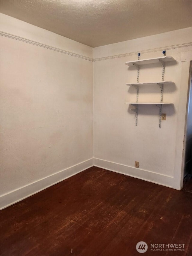 spare room featuring dark wood finished floors, a textured ceiling, and baseboards