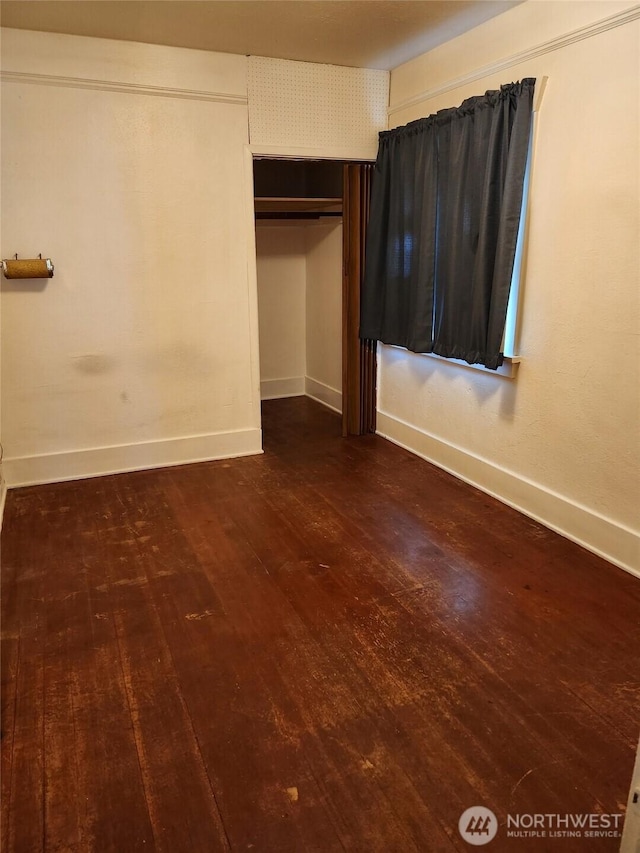 unfurnished bedroom featuring baseboards, dark wood finished floors, and a closet