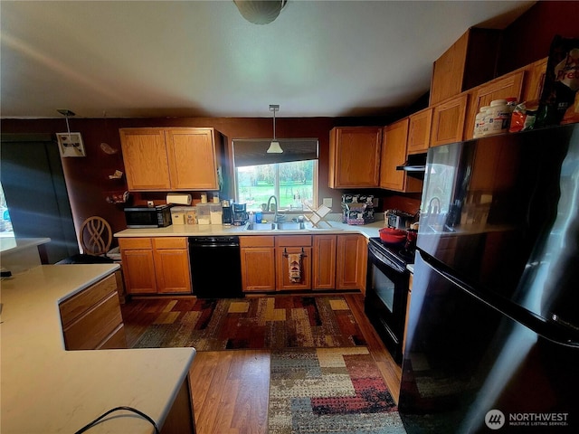 kitchen featuring dark wood finished floors, decorative light fixtures, light countertops, black appliances, and a sink