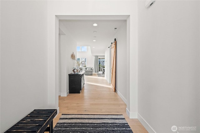 hall featuring light wood-style floors, recessed lighting, baseboards, and a barn door