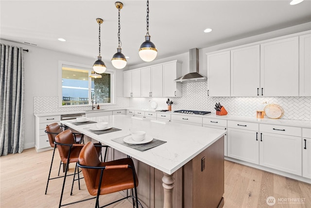 kitchen featuring gas cooktop, a sink, a kitchen island, a kitchen breakfast bar, and wall chimney range hood