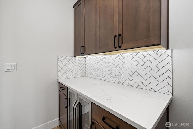 kitchen featuring baseboards, backsplash, dark brown cabinetry, and light stone countertops