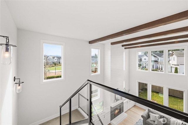 corridor featuring beamed ceiling, wood finished floors, an upstairs landing, and baseboards