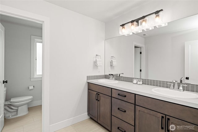 bathroom featuring baseboards, a sink, toilet, and double vanity