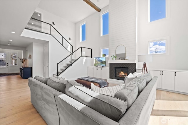 living room with a fireplace, light wood finished floors, a towering ceiling, a healthy amount of sunlight, and stairs