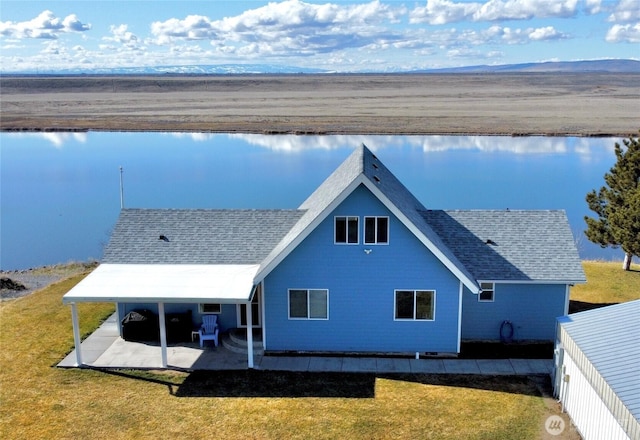 back of property with a patio, a yard, roof with shingles, and a water view