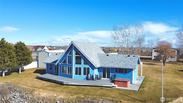 back of property with a deck, roof with shingles, and a hot tub