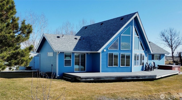 rear view of house with a shingled roof, a lawn, and a deck