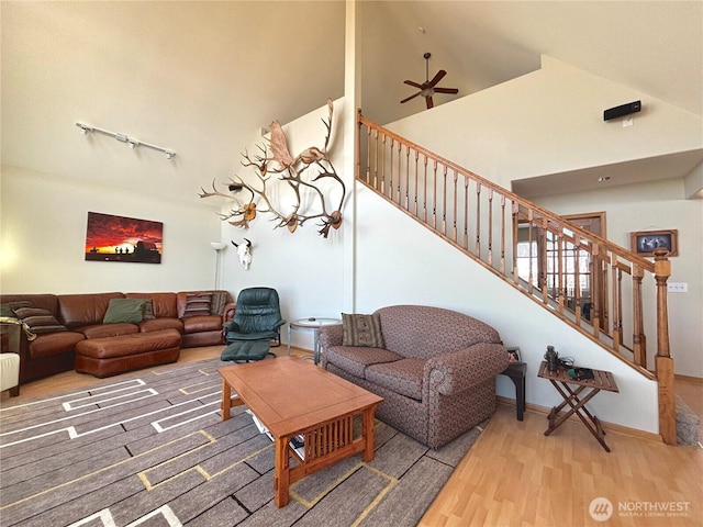 living room featuring baseboards, a ceiling fan, stairway, wood finished floors, and high vaulted ceiling