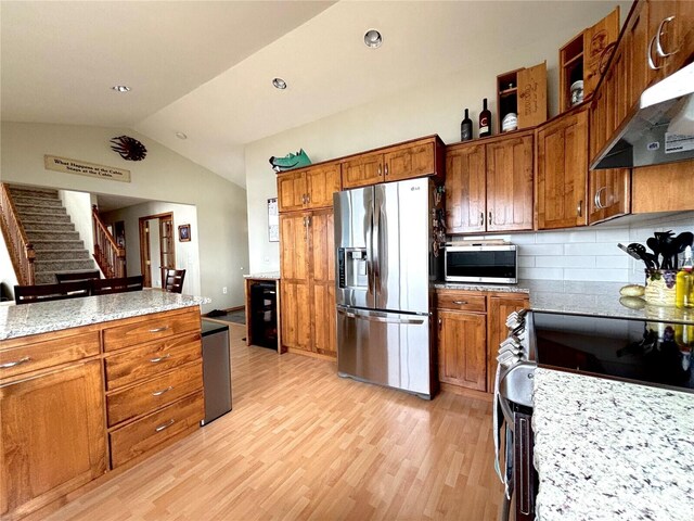 kitchen with lofted ceiling, extractor fan, light wood-style flooring, stainless steel appliances, and brown cabinetry