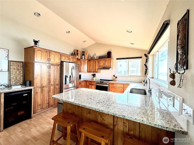 kitchen featuring lofted ceiling, a peninsula, a sink, appliances with stainless steel finishes, and light stone countertops