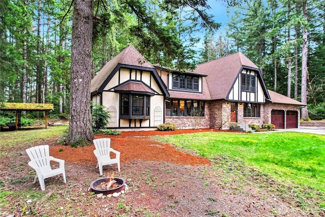 tudor house with driveway, a fire pit, roof with shingles, a front yard, and stucco siding