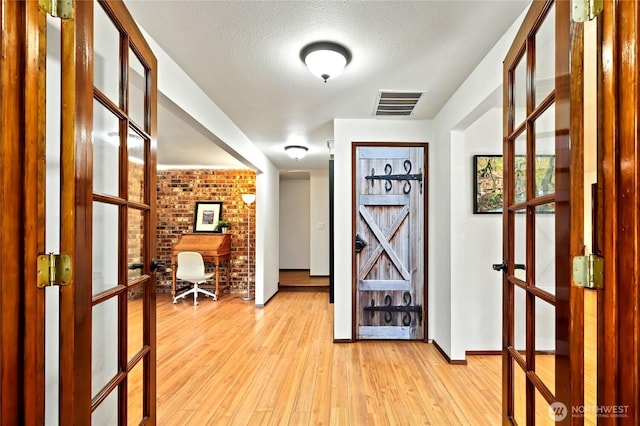 doorway with french doors, visible vents, light wood-style flooring, a textured ceiling, and brick wall