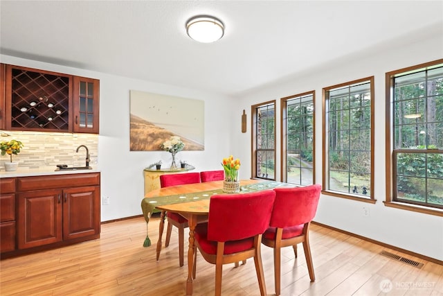 dining area with light wood-style floors, visible vents, a wealth of natural light, and indoor wet bar