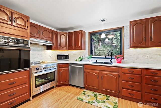 kitchen featuring under cabinet range hood, stainless steel appliances, a sink, light countertops, and light wood finished floors