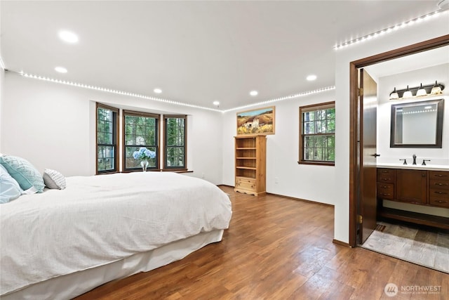 bedroom featuring recessed lighting, a sink, wood finished floors, baseboards, and ensuite bath