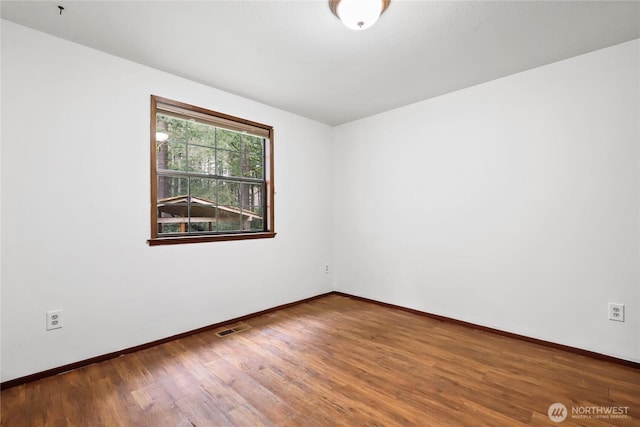 spare room featuring wood finished floors, visible vents, and baseboards