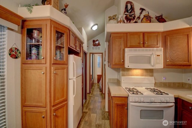 kitchen with white appliances, light wood finished floors, glass insert cabinets, vaulted ceiling, and light countertops