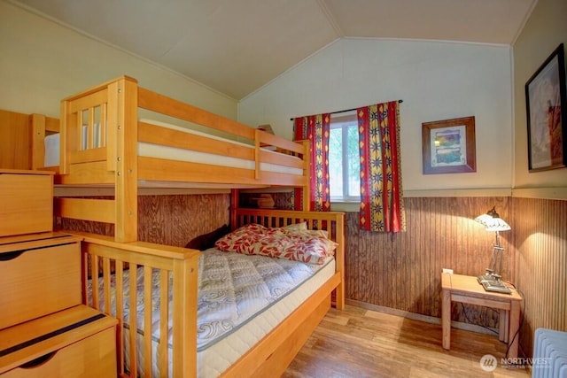 bedroom with a wainscoted wall, wood walls, wood finished floors, vaulted ceiling, and radiator