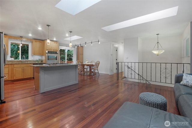 kitchen featuring a skylight, open floor plan, a center island, light brown cabinetry, and pendant lighting