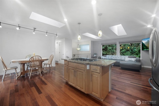 kitchen featuring a skylight, a kitchen island, appliances with stainless steel finishes, decorative light fixtures, and light stone countertops