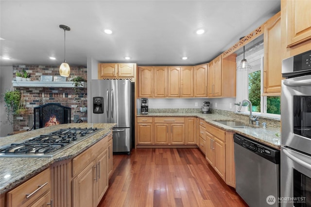 kitchen with stainless steel appliances, a sink, hanging light fixtures, and light brown cabinetry