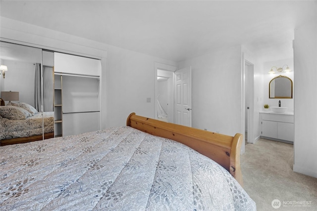 bedroom featuring a closet, light colored carpet, a sink, ensuite bath, and baseboards