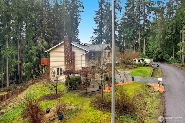 view of side of property with driveway, a chimney, and a yard