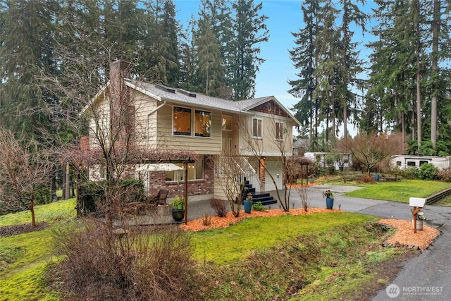 split foyer home with brick siding, concrete driveway, a chimney, an attached garage, and a front yard