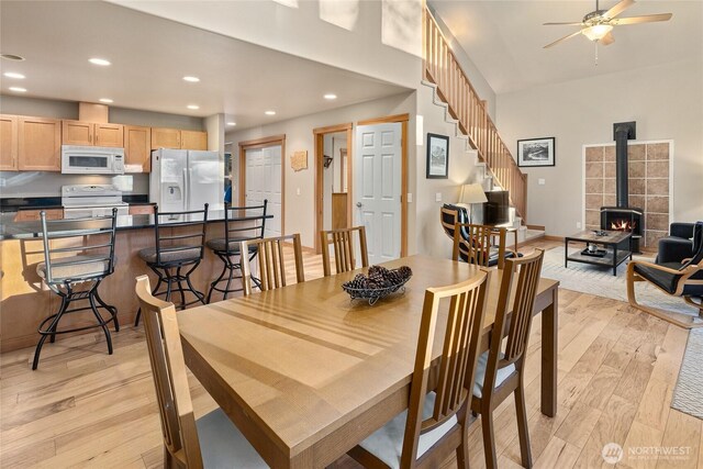 dining area with light wood finished floors, ceiling fan, a wood stove, stairs, and recessed lighting