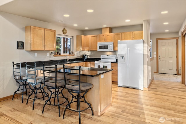 kitchen with white appliances, a kitchen breakfast bar, a peninsula, light brown cabinets, and a sink