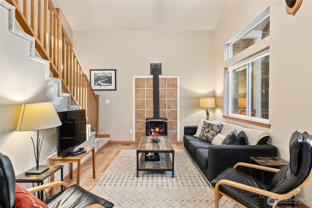 living room featuring stairway, wood finished floors, a wood stove, and baseboards